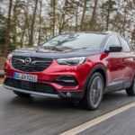 Se ve un SUV Opel rojo, conocido por su desempeño y confort, conduciendo por una tranquila carretera rural.
